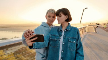 Köprüde dikilen lezbiyen çift güneşin doğuşunu izlerken selfie çekiyorlar.
