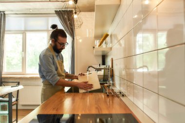 Genç adam, İtalyan aşçı sebze doğradıktan sonra lavaboda tahtaları yıkıyor.