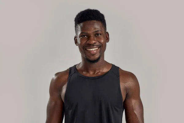 Homem americano africano muscular jovem sorrindo para a câmera enquanto posando isolado sobre fundo cinza. Esportes, treino, conceito de musculação — Fotografia de Stock
