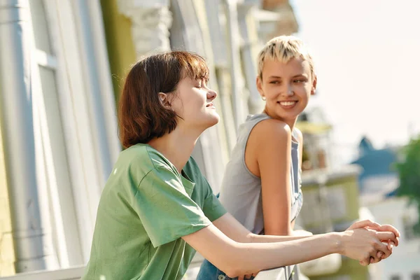 Portrét mladé ženy těší slunce, zatímco stojí na balkóně se svou přítelkyní. Lesbičky pár tráví svůj den spolu — Stock fotografie