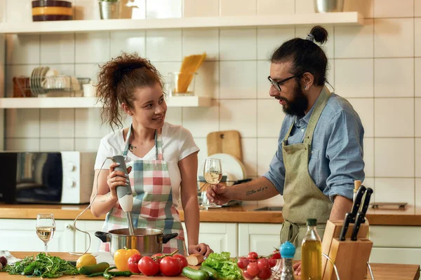 Молода пара готує вечерю разом на кухні. Італієць, шеф-кухар, дивиться на свою подругу, тримаючи склянку білого вина. Куховарство вдома, італійська кухня. — стокове фото