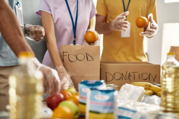 Acercamiento de manos de voluntarios en la recolección de guantes, clasificación de alimentos para personas necesitadas en bolsas de papel, Equipo trabajando juntos en el proyecto de donación — Foto de Stock