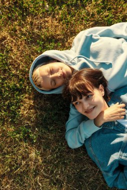 Yaz parkında çimlerin üzerinde yatan mutlu lezbiyen çift manzarası. Aşık kadınlar, dışarıda birlikte vakit geçiriyorlar.