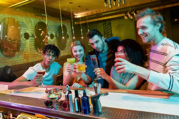 A fazer memórias. Grupo de amigos, jovens adultos, homens e mulheres se divertindo enquanto brindam, bebendo coquetéis no balcão do bar na boate — Fotografia de Stock