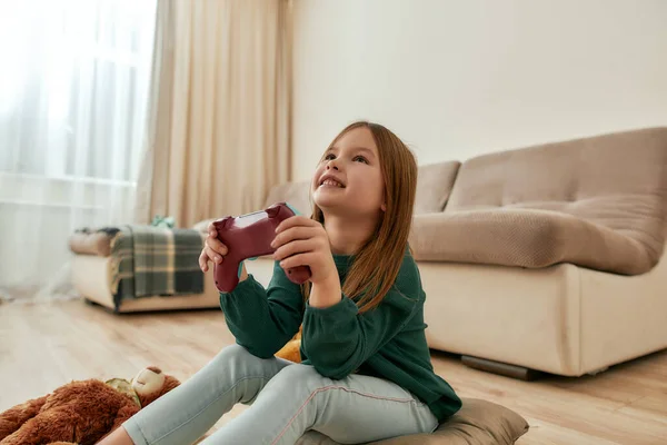 En liten söt flicka njuta av att spela videospel leende hålla en gamepad medan du sitter på ett golv — Stockfoto