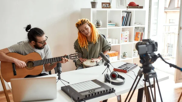 Music is art. Man playing guitar and woman playing rhythm with djembe drum while recording video blog or vlog. Couple of musicians making music at home. — Stock Photo, Image