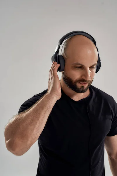 A ouvir música. Retrato de jovem homem forte muscular usando fones de ouvido em pé isolado sobre fundo cinza — Fotografia de Stock