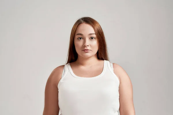 Ritratto di una bella giovane caucasica plus size donna vestita di camicia bianca, che guarda la macchina fotografica mentre posa isolata su sfondo grigio — Foto Stock