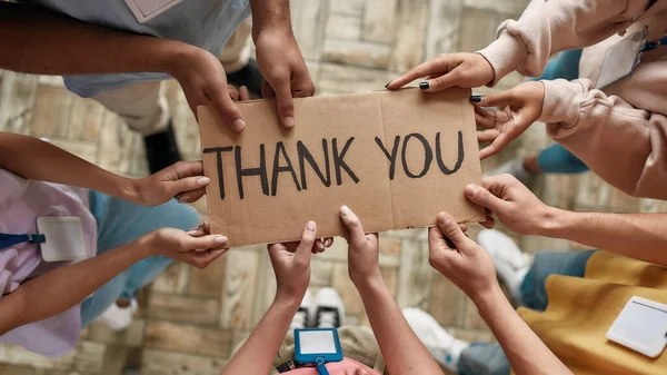 Вид сверху на разношерстных молодых волонтеров, держащих в руках удостоверение с благодарностью, стоя в офисе благотворительной организации — стоковое фото