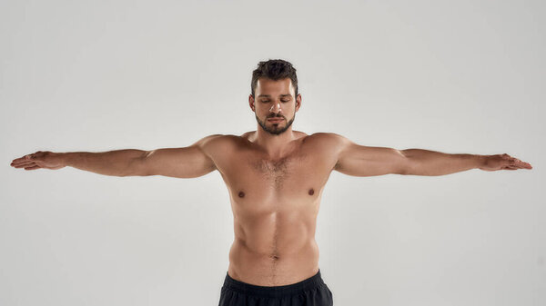 Готов к плаванию. Молодой спортсмен с обнаженным туловищем закрывает глаза, позируя с протянутыми руками, изолированными на сером фоне.