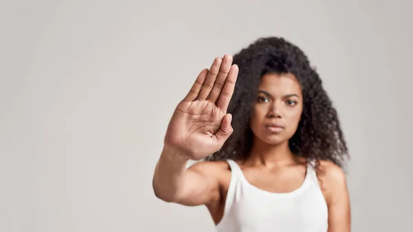 Retrato de una joven afroamericana con cabello rizado con camisa blanca que tiene un aspecto serio y confiado mientras muestra, haciendo un gesto de stop aislado sobre fondo gris — Foto de Stock