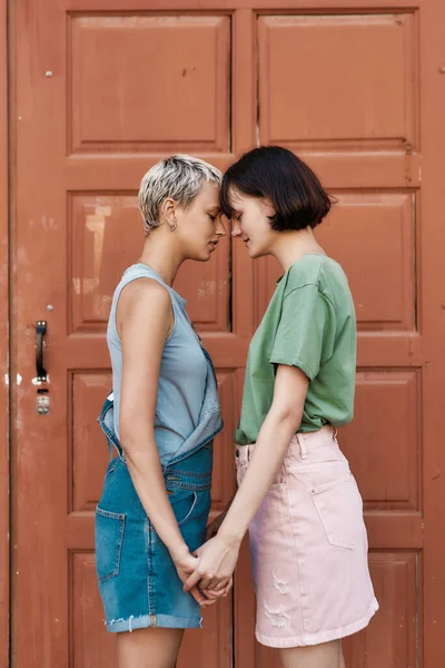 Momento emotivo. Giovane coppia femminile, due donne che toccano la fronte, tenendosi per mano in piedi davanti alla porta all'aperto — Foto Stock