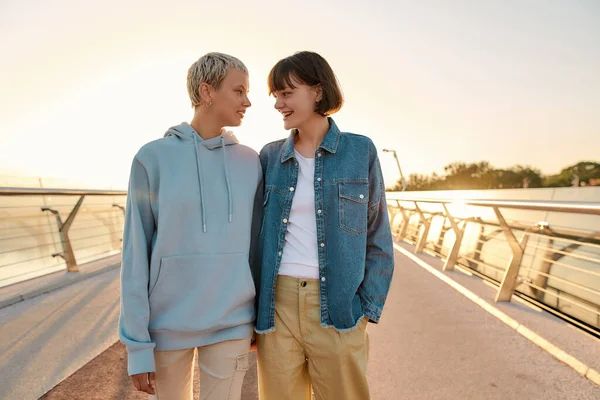 Gelukkig lesbisch stel dat elkaar aankijkt terwijl ze over de brug lopen en samen naar de zonsopgang kijken. Homoseksualiteit, LGBT en liefdesconcept — Stockfoto