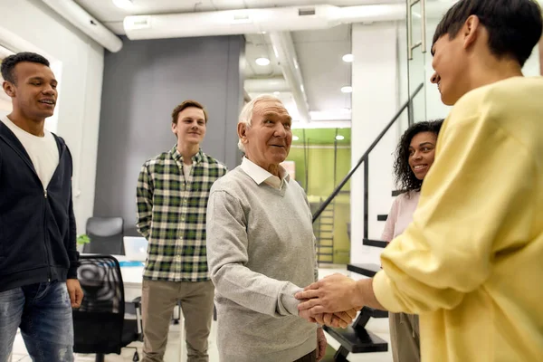 Fröhliches junges Team begrüßt neue Mitarbeiter im modernen Büro, älterer Mann oder Senior-Praktikant beim Händeschütteln mit Kollegen — Stockfoto