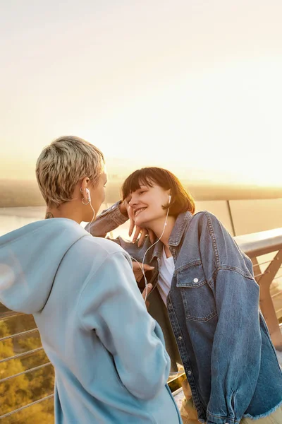 Young lesbian couple having romantic moment while listening to music sharing one same earphones, Two women smiling at each other, spending time together outdoors — Stock Photo, Image