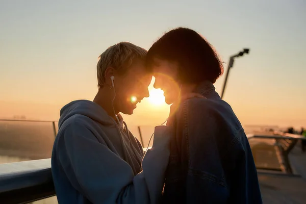 Young lesbian silhouetted couple, two happy women having romantic moment while listening to music sharing one same earphones — Stock Photo, Image