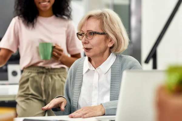 Close up of aged woman, senior intern talking to her young colleagues, Friendly workers listening to new employee during coffee break at work — Stock Photo, Image