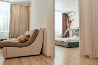 Parlak bir yatak odasındaki büyük bir yatakta yalınayak zıplayan küçük bir kız.