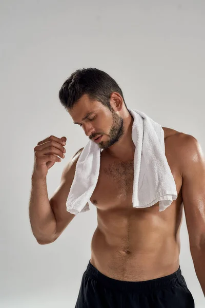 So exhausted. Portrait of young athletic man with towel on his shoulders resting after training, looking aside while standing isolated over grey background — Stock Photo, Image