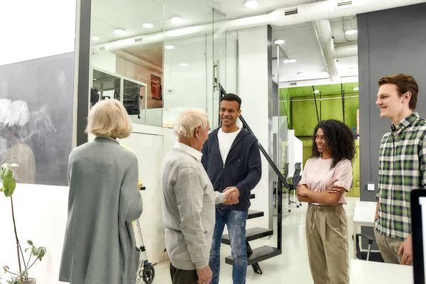 Vrolijke jonge team begroeten nieuwe medewerkers, Verouderde man en vrouw, senior stagiaires schudden handen met collega 's in het moderne kantoor — Stockfoto