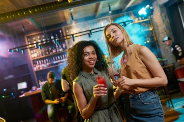 Geceyi burada hisset. Çekici genç kadınlar kameraya bakıp ellerinde kokteyl ile poz veriyorlar. Arkadaşlar kutluyor, barda eğleniyorlar.