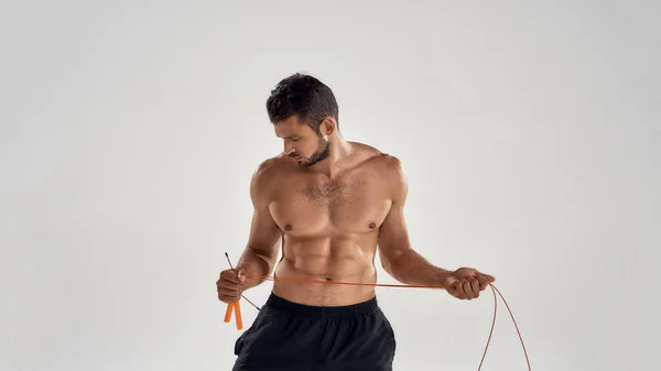 Mode de vie sain et actif. Jeune homme athlétique en tenue de sport tenant une corde à sauter tout en étant isolé sur fond gris — Photo