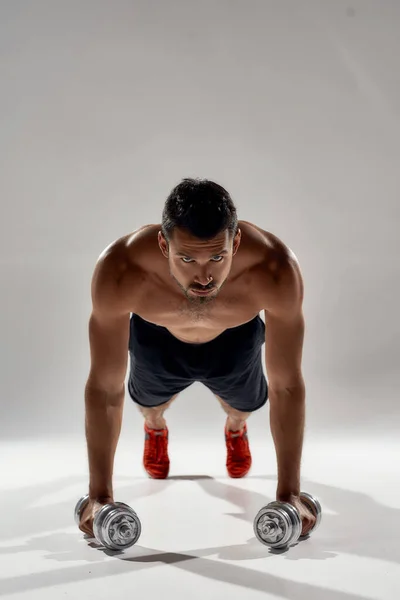 A treinar. Jovem homem atlético forte fazendo flexões em pesos isolados sobre fundo cinza — Fotografia de Stock