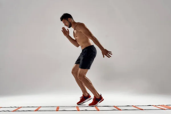 Fitness trénink. Plná délka záběr mladého atletického muže trénink na agility žebřík vrták izolované přes šedé pozadí — Stock fotografie