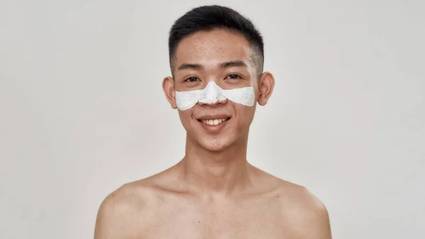 Retrato de jovem asiático sem camisa com pele problemática e hiperpigmentação aplicada máscara em seu rosto, sorrindo para câmera isolada sobre fundo branco. Beleza, rotina de cuidados da pele — Fotografia de Stock