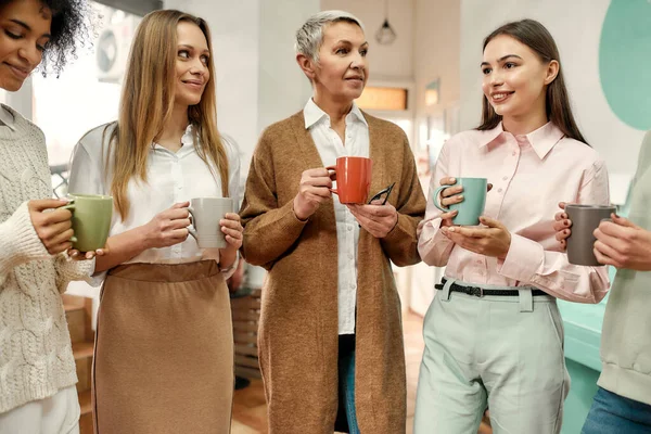 Cinque donne ben vestite di età diversa che fanno una pausa caffè mattutina durante un brainstorming — Foto Stock