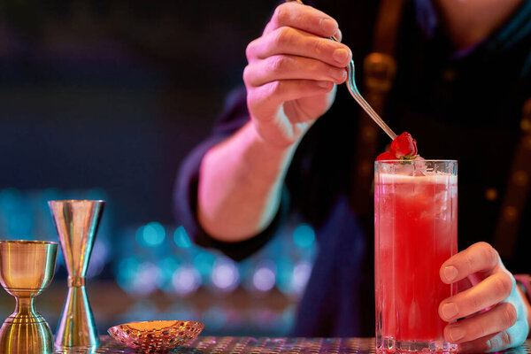 Get a drink. Close up of bartender hand decorating cocktail in glass with rose flower while making alcoholic drink at the bar counter in the night club