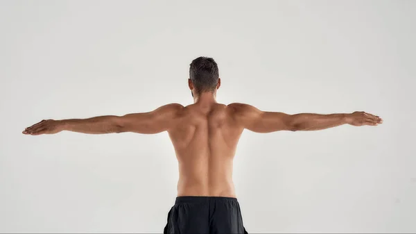 Вид сзади на мускулистого человека с обнаженным туловищем, позирующим с вытянутыми руками на сером фоне — стоковое фото