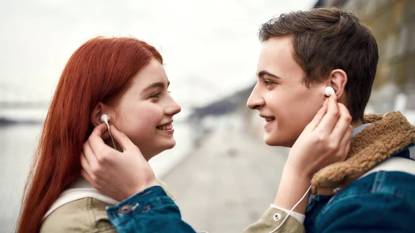 Close-up van een paar tieners gaan naar muziek te luisteren met behulp van hetzelfde paar oortelefoons, kijken naar elkaar met liefde — Stockfoto