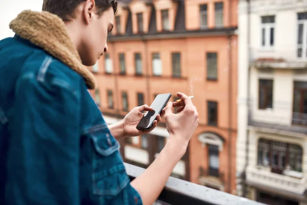 Έφηβος καπνίζει και χρησιμοποιεί το κινητό του τηλέφωνο ενώ στέκεται στο μπαλκόνι — Φωτογραφία Αρχείου