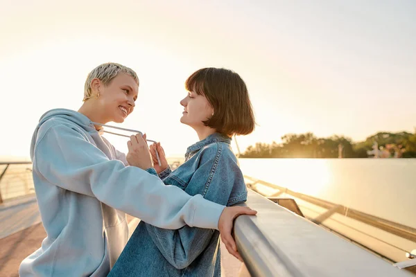 A game of heart. Lesbian couple looking at each other with a smile before kissing, leaning on the bridge while watching the sunrise together. Homosexuality, LGBT and love concept — Stock Photo, Image