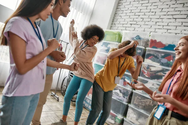 Fröhlich bunte junge Ehrenamtliche tanzen, haben Spaß und feiern Erfolge im karitativen Organisationsbüro — Stockfoto