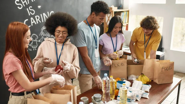 幸せな若いボランティアグループが集まり、紙袋で食べ物を分類し、慈善団体事務所で寄付プロジェクトに取り組む多様なチーム — ストック写真