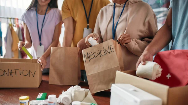 Recorte de grupo de voluntarios empacando la donación de medicamentos en bolsas de papel y cajas para personas necesitadas, equipo pequeño que trabaja en la fundación benéfica — Foto de Stock