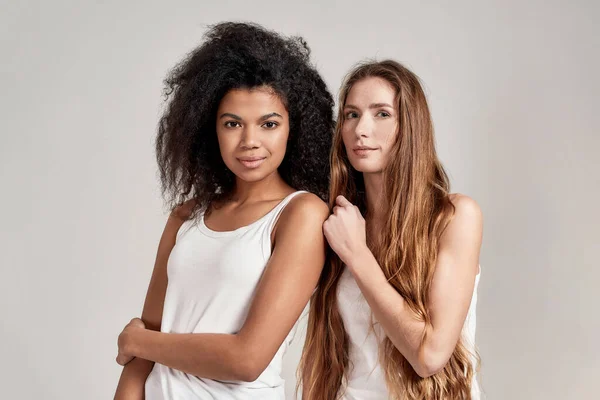 Πορτρέτο δύο νεαρών γυναικών με λευκά πουκάμισα που κοιτούν την κάμερα ενώ ποζάρουν μαζί απομονωμένες σε γκρι φόντο — Φωτογραφία Αρχείου