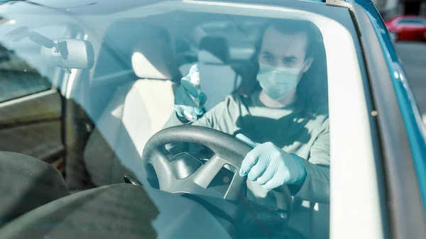 Man met medisch masker en beschermende handschoenen die antibacteriële desinfecterende spray op het stuur spuiten terwijl hij het interieur van de auto reinigt om virussen te voorkomen — Stockfoto