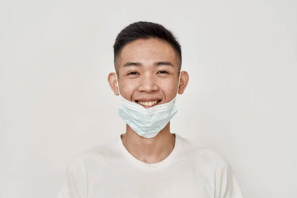 Retrato de jovem asiático homem sorrindo para a câmera enquanto tem máscara médica em seu queixo isolado sobre fundo branco. Saúde, prevenção, conceito de segurança — Fotografia de Stock