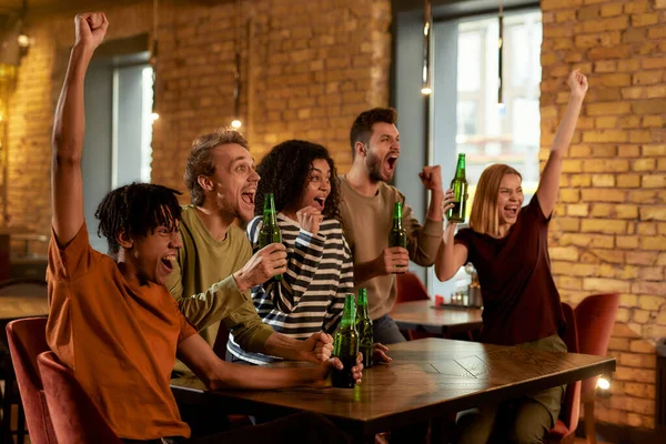 Amigos felices en el bar viendo partidos deportivos en la televisión juntos, bebiendo cerveza y animando al equipo — Foto de Stock