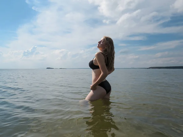 A young beautiful woman in a black bikini with a full bust is bathing in the sea