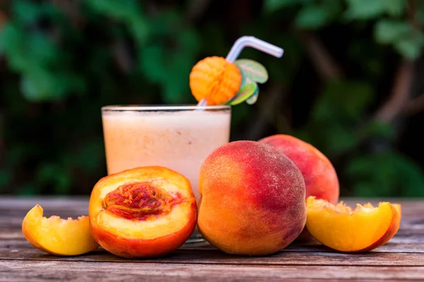 Glass of peach yoghurt and peaches on wooden table — Stock Photo, Image