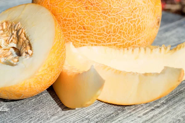 Whole and sliced melon on wooden table outdoors