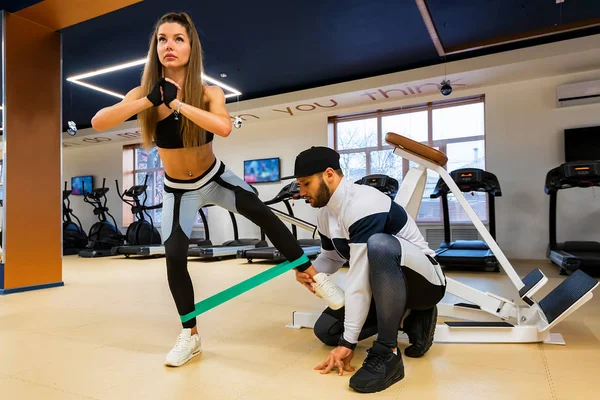 Entrenador personal que entrena al culturista femenino con banda elástica en el gimnasio moderno — Foto de Stock