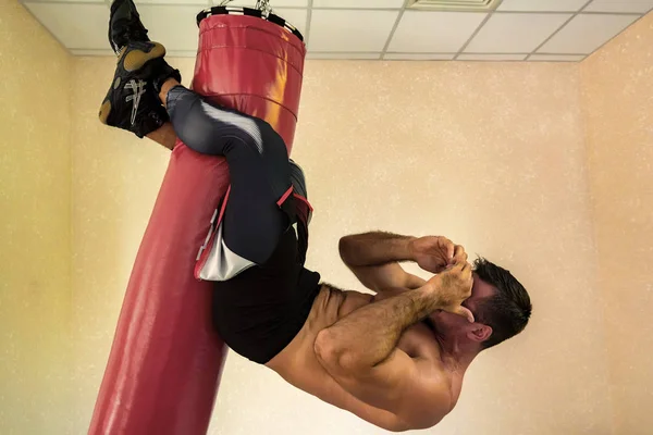 Prise de vue d'un jeune homme en forme travaillant abdos tout en accrochant sur le sac de boxe — Photo
