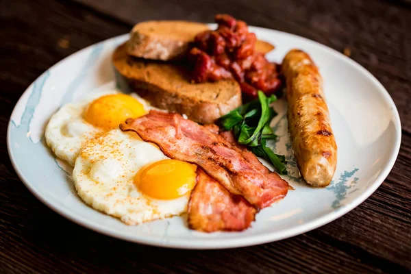 Pequeno-almoço típico com ovos, bacon e salsicha no prato — Fotografia de Stock