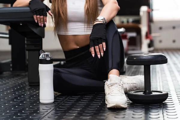 Atractivo modelo de fitness se sienta con bebida de fitness en el gimnasio moderno. Vista de la parte inferior — Foto de Stock