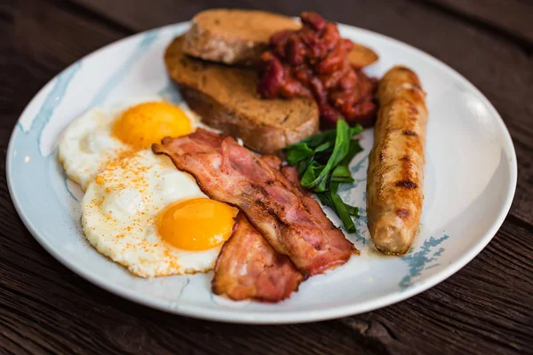 Pequeno-almoço típico com ovos, bacon e salsicha no prato — Fotografia de Stock